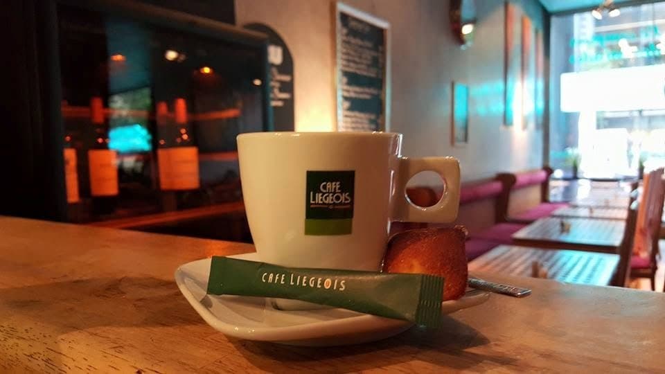 Une tasse de café sur le comptoir en bois ; derrière, la salle, ses tables et ses banquettes rouges le long du mur