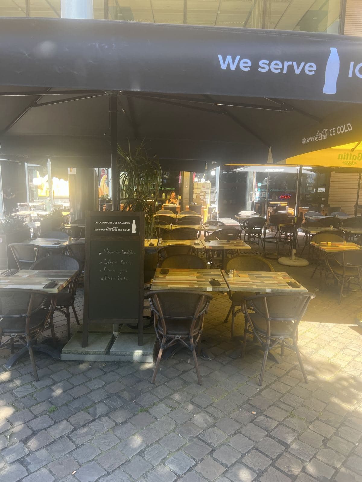La terrasse en plein soleil sous de grands parasols noirs, les tables dressées sur les pavés de la place, l'ardoise du restaurant à l'entrée