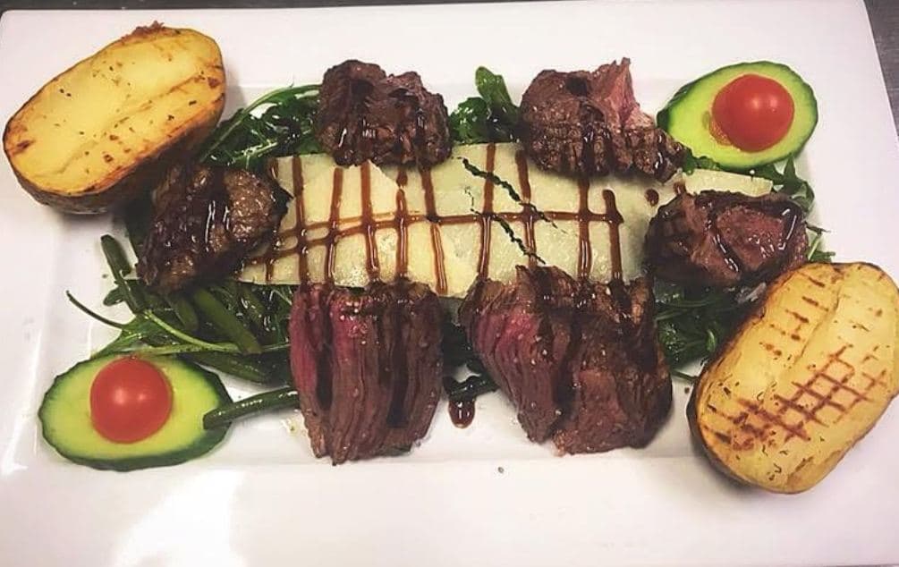 Des médaillons de bœuf grillé alignés sur la roquette, entre deux demi-avocats et deux pommes de terre grillées