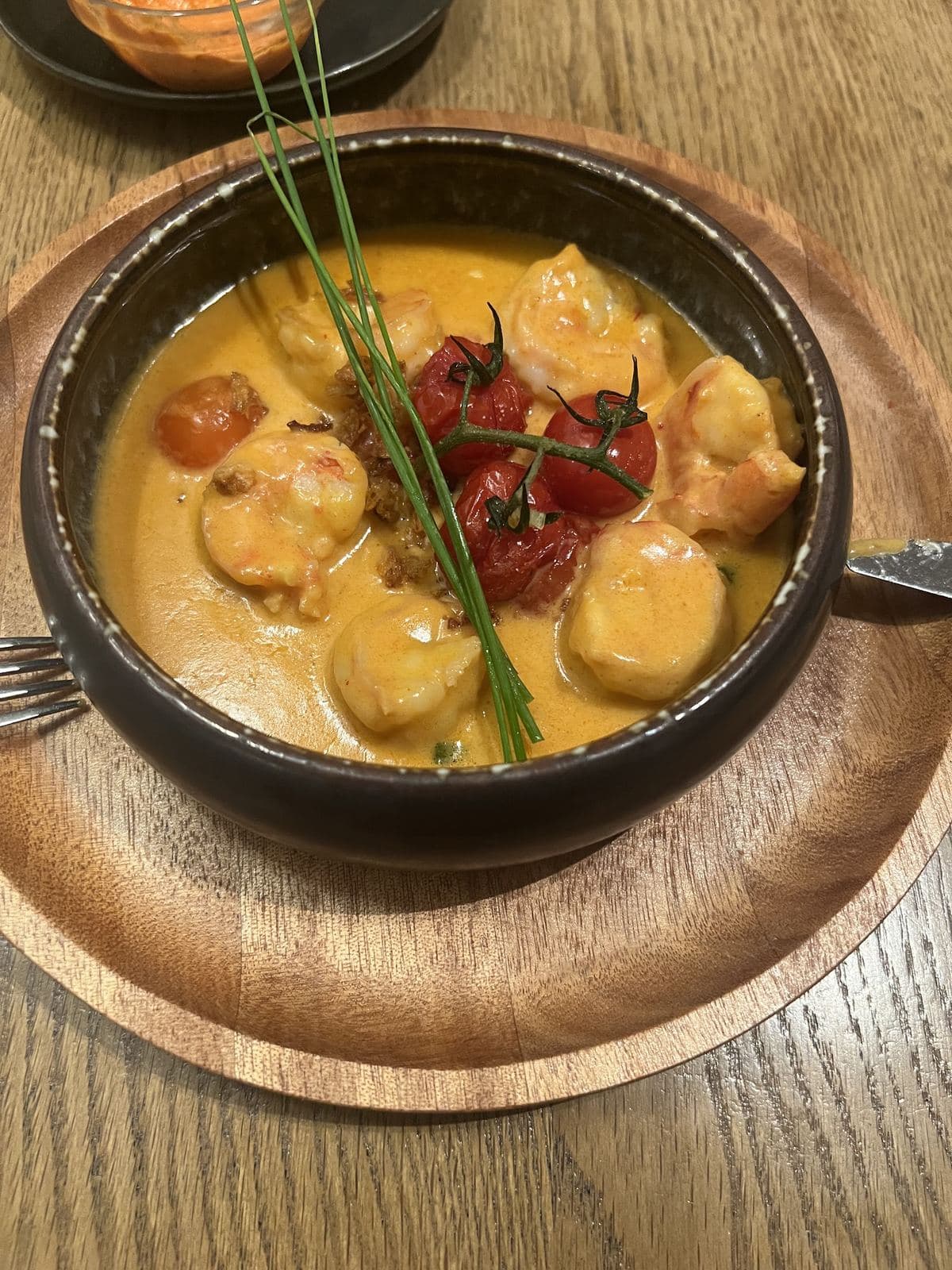 Des noix de Saint-Jacques et des scampis dans une sauce orangée, avec des tomates cerise rôties, servis dans une cassolette noire