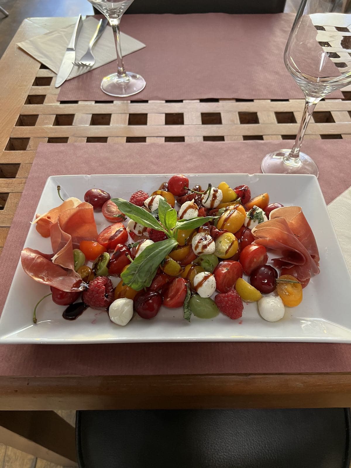 Des tomates cerise de toutes les couleurs, des billes de mozzarella et du jambon cru sur un plat blanc, en terrasse