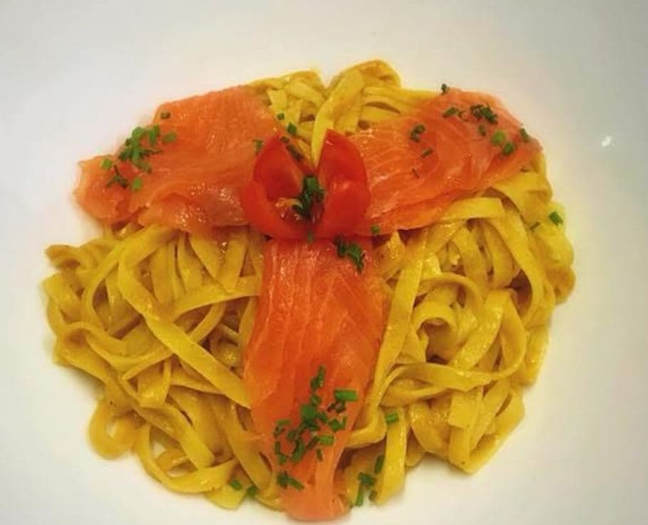 Un nid de tagliatelles couvert de lamelles de saumon fumé et d'une fleur de tomate